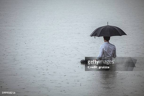 handsome man standing in water and holding umbrella during rain - depressie landelement stockfoto's en -beelden