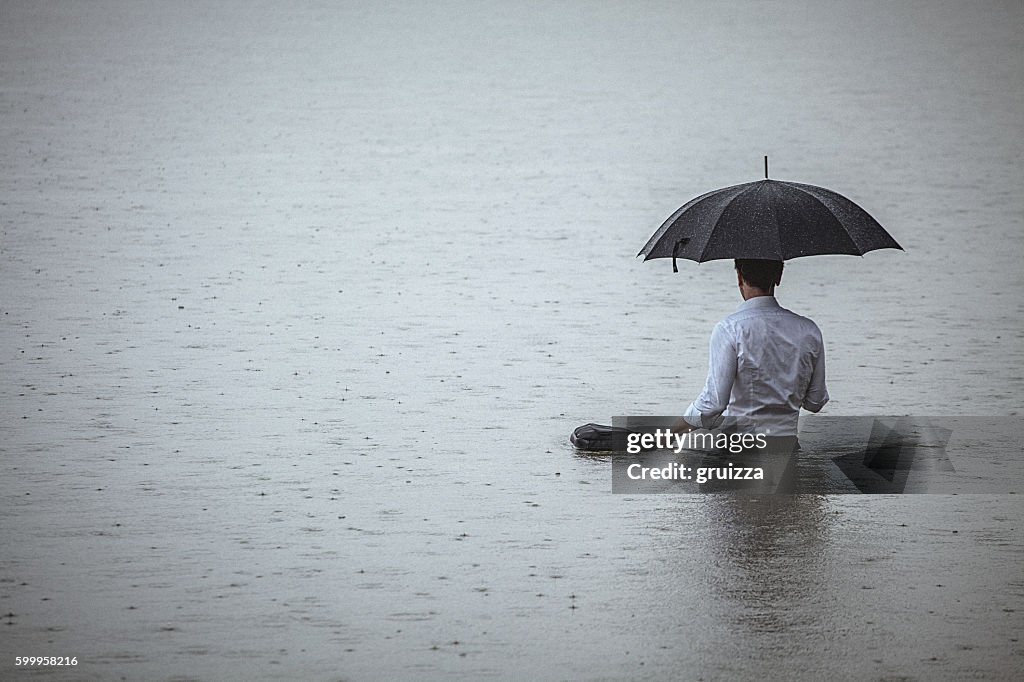 Handsome man standing in water and holding umbrella during rain