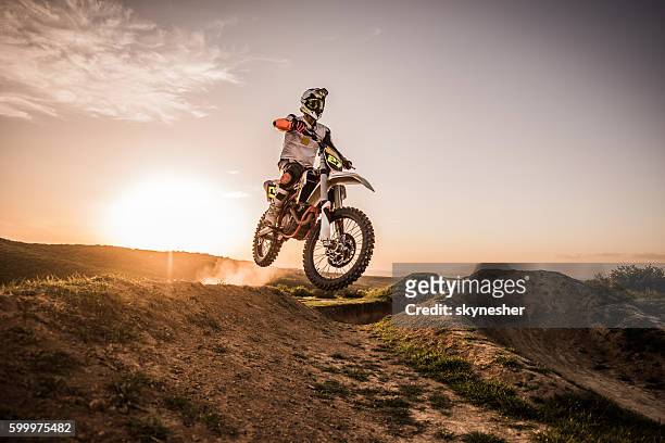 dirt bike racer at sunset performing jump on dirt road. - dirt road motorbike stock pictures, royalty-free photos & images