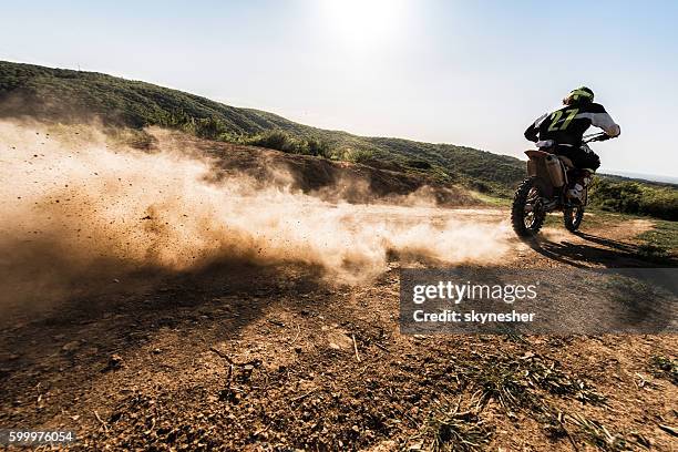 rückansicht des motocross-fahrers, der schnell auf felduneinigem weg fährt. - dirt road motorbike stock-fotos und bilder