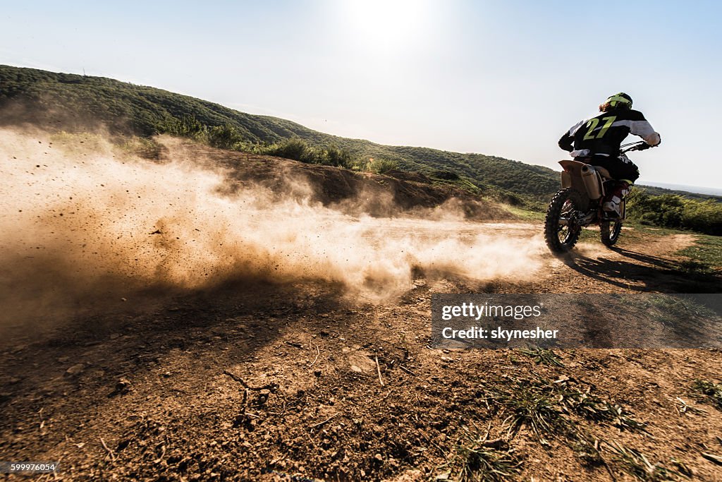 Back view of motocross rider driving fast on dirt track.