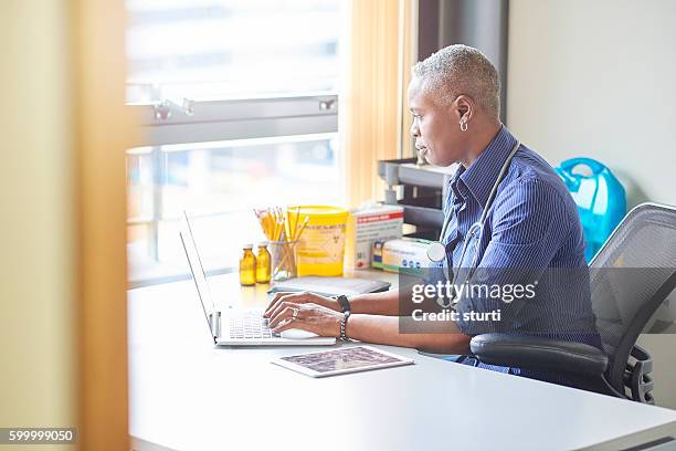female doctor sitting at her desk - general practitioner stock pictures, royalty-free photos & images