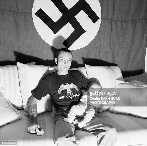 Member of Ku Klux Klan holding his baby in front of a flag baring the swastika.