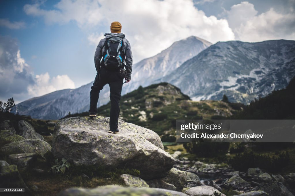 Traveler with backpack looks on a mountain peak
