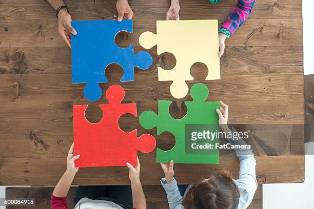 putting together puzzle pieces - four people stockfoto's en -beelden