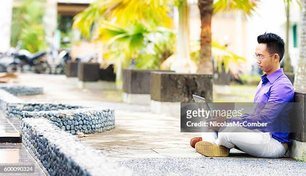 ラップトップで屋外に座っている陰茎インドネシアの男子学生 - インドネシア人 ストックフォトと画像