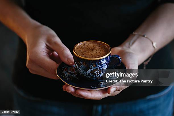 a woman is holding a cup of turkish coffee with foam on top (with both hands). photographed from the front. - turkish coffee stock pictures, royalty-free photos & images