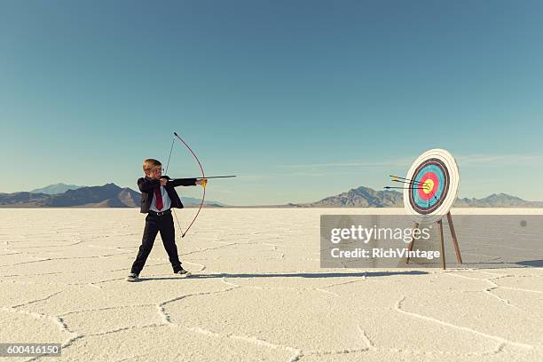 young boy businessman shoots arrows at target - pijl en boog stockfoto's en -beelden