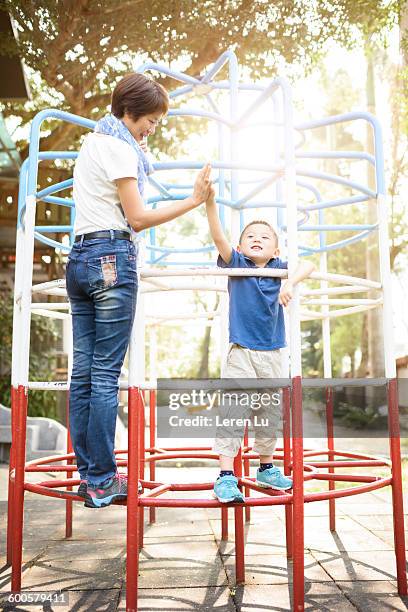 mom and kid clasping hands on jungle gym - mother and son at playground stock-fotos und bilder