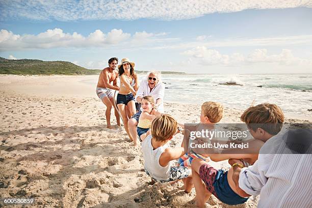 family and friends playing tug of war on beach - forte beach photos et images de collection