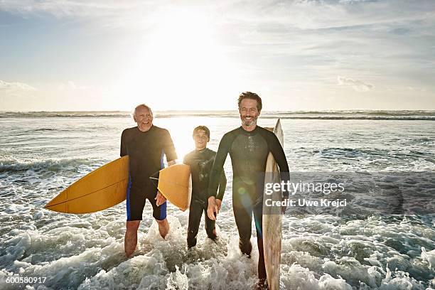 three generations of surfers on beach - mature surfers stock pictures, royalty-free photos & images