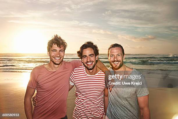 three male friends on beach, smiling - friends male stock-fotos und bilder