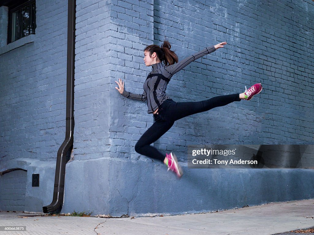 Young woman in athletic wear jumping near wall