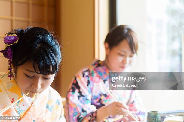 kimono wearing young japanese women eating noodles in a restaurant - geisha eating stockfoto's en -beelden