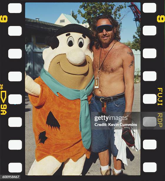 Bassist Peter Hook of English rock group New Order with a person in a Fred Flintstone costume, at the Canada's Wonderland theme park in Vaughan,...