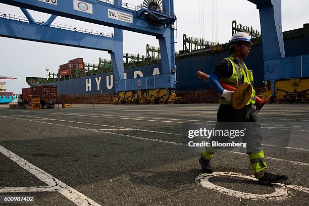 An employee wearing a hi-vis jacket and a hard hat walks past Hyundai Merchant Marine Co.'s Hyundai Forward container ship at a container terminal at...