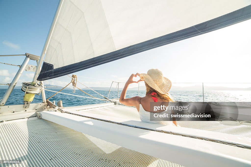 Woman on sailing boat makes heart shape finger frame