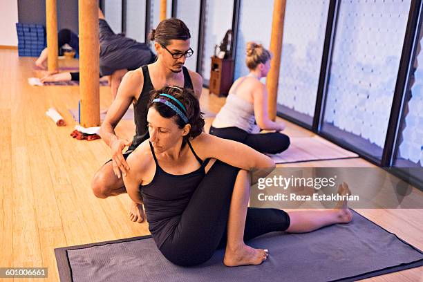 teacher adjusts student in marichyasana - spinal twist stock pictures, royalty-free photos & images