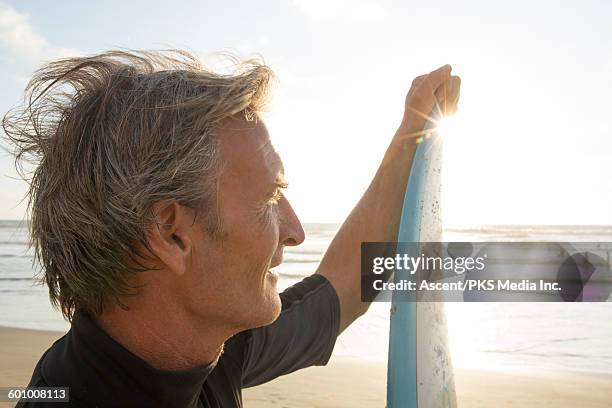 mature man holds surfboard after surfing,looks off - first gray hair stock pictures, royalty-free photos & images