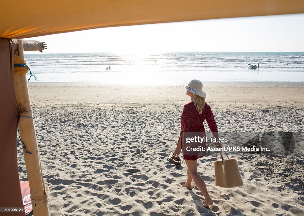 View past beach canopy to woman carrying beach bag