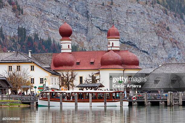 Boat with tourists in front of the Sankt Bartholoma / St. Bartholomew's Church at lake Konigssee, Berchtesgaden National Park, Bavaria, Germany.