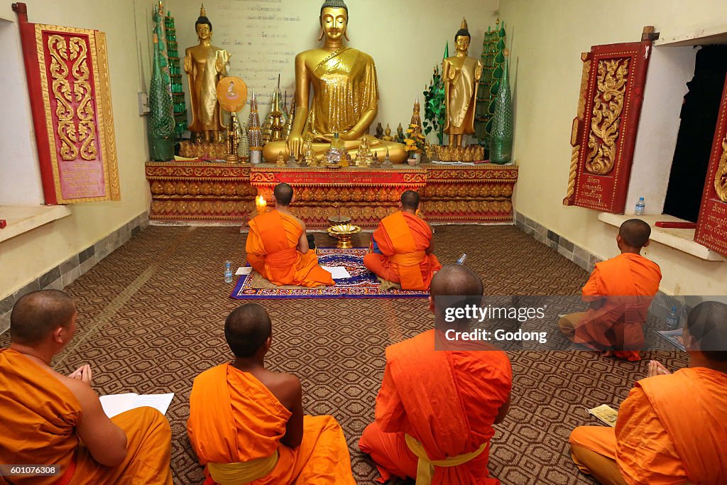 Group of seated, young Buddhist monks chanting and reading prayers at a ceremony.