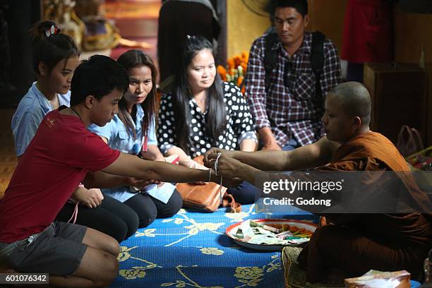 Wat Si Muang buddhist temple. Buddhist ceremony. Monk ties blessed cotton bracetet around a wrist. Vientiane, Laos.