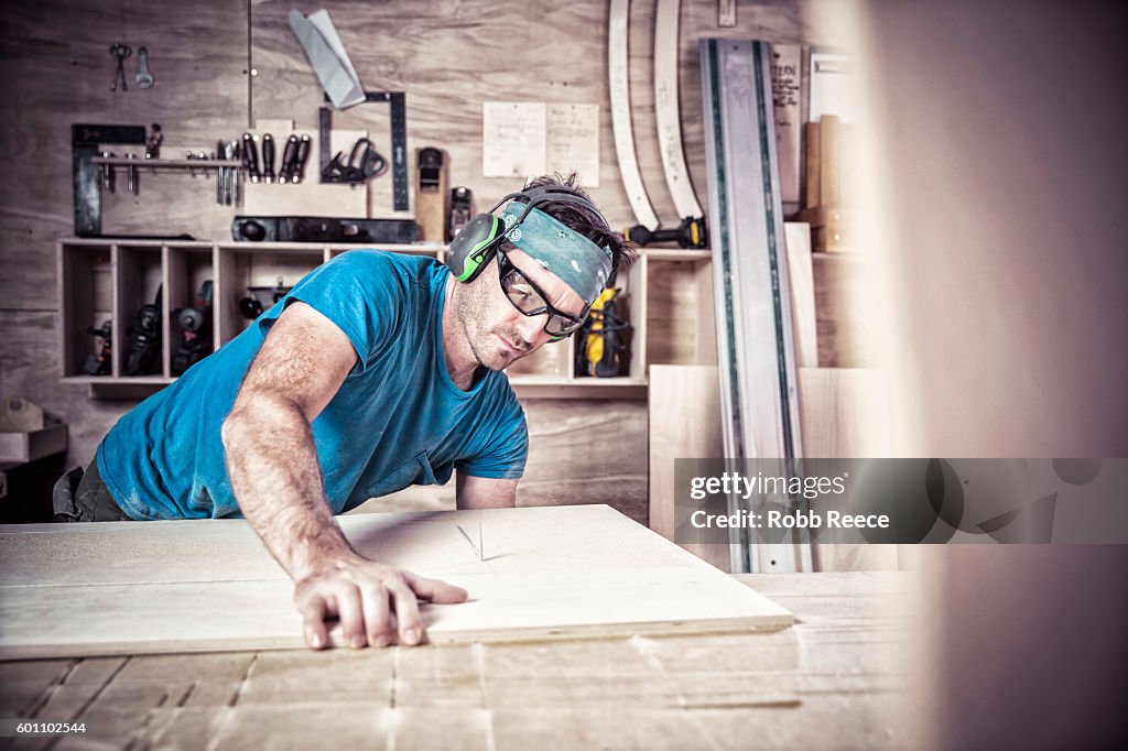 An adult, male carpenter working with tools in his wood shop