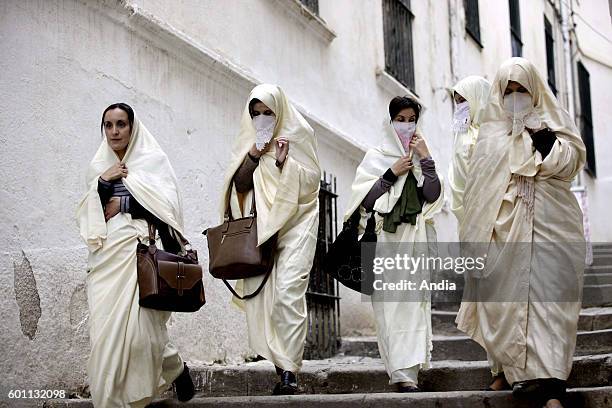 Group of women wearing haiks, long white embroidered gowns, Algerian women's traditional dress, walking in a lane of Algiers kasbah. .