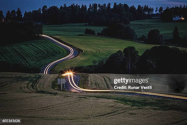 long exposure of car driving on a curvy road in the countryside. - farm norway stock pictures, royalty-free photos & images