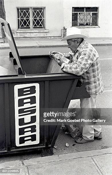 An elderly man looks at a bottle of liquor found in a garbage bin , Juarez, Mexico, late 1980s.