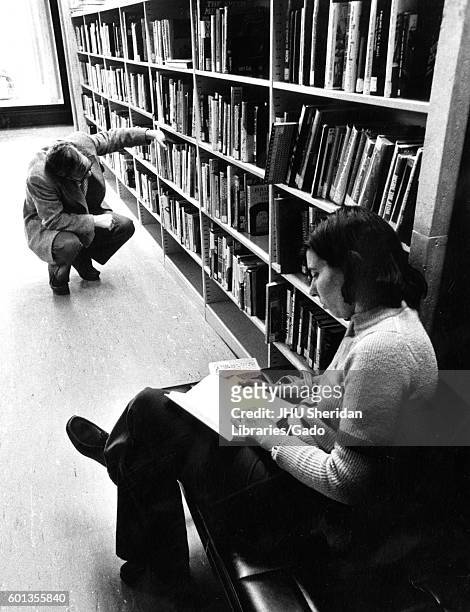 Candid portrait of two Johns Hopkins University students sitting in the stacks reading and looking for books in the University's Milton S Eisenhower...