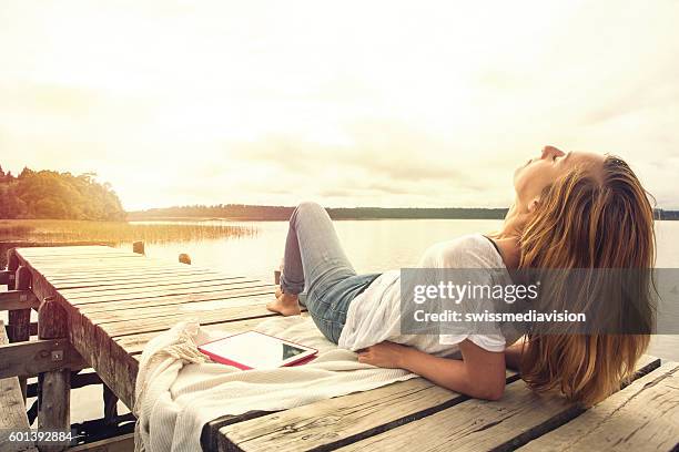 caucasian girl lies on jetty above lake at sunset - jetty stock pictures, royalty-free photos & images