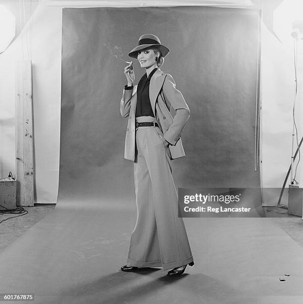 French fashion - a trouser suit by Yves Saint Laurent in stone gabardine with a double-breasted jacket, green crepe-de-chine shirt and stone felt...