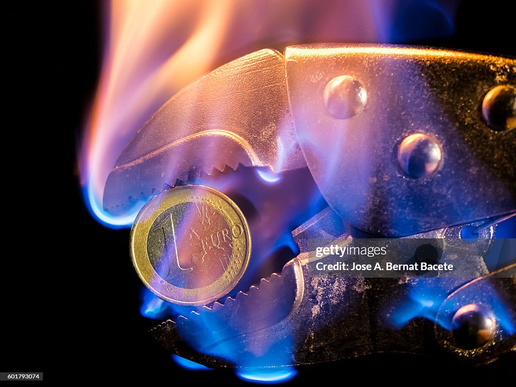 Tool in the shape of tweezer holding a currency of incandescent Euro for the fire
