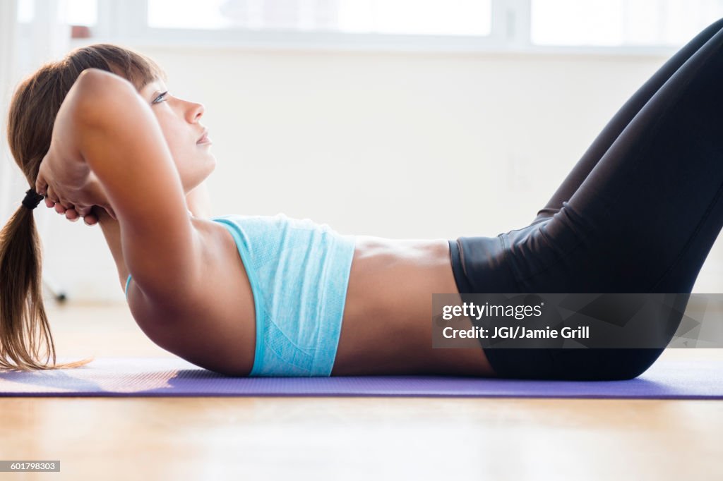 Mixed race woman doing sit-ups on yoga mat