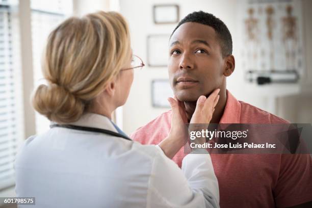 doctor examining throat of patient in clinic - hombre revision fotografías e imágenes de stock