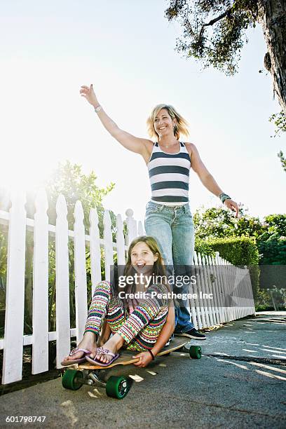 caucasian mother and daughter riding skateboard on sidewalk - longboard stock-fotos und bilder