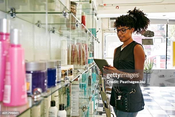 mixed race hairstylist using digital tablet in salon - hair products fotografías e imágenes de stock