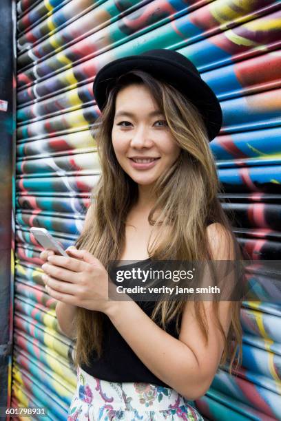 asian woman using cell phone near graffiti wall - graffiti wall london stock-fotos und bilder