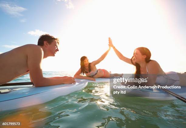 friends high-fiving on paddle boards in ocean - junge 13 jahre oberkörper strand stock-fotos und bilder