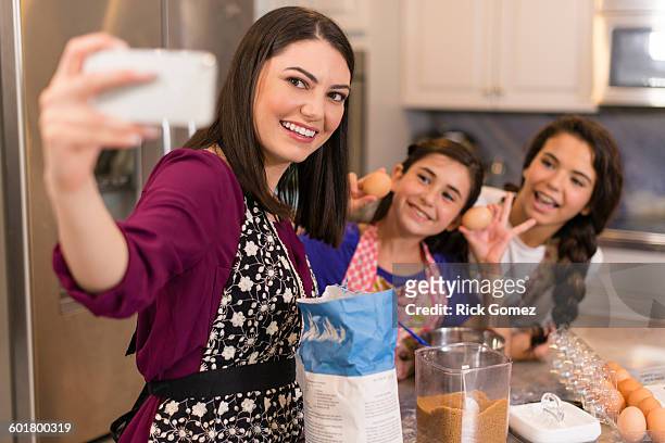 mother and daughters taking selfie in kitchen - young women group back stock-fotos und bilder