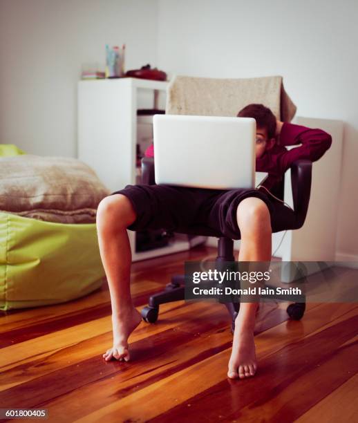 mixed race boy using laptop in chair - mala postura fotografías e imágenes de stock