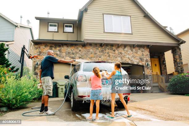 father and daughters washing car - car in driveway stock-fotos und bilder