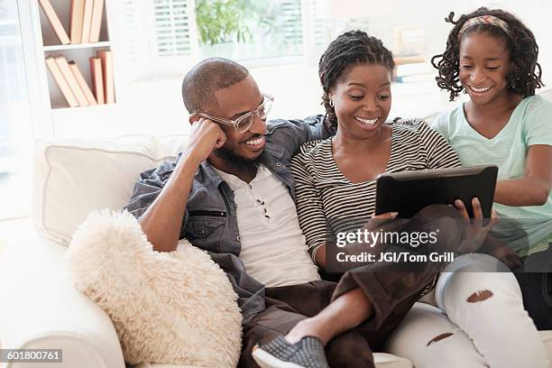 black family using digital tablet on sofa - men women & children film stock-fotos und bilder