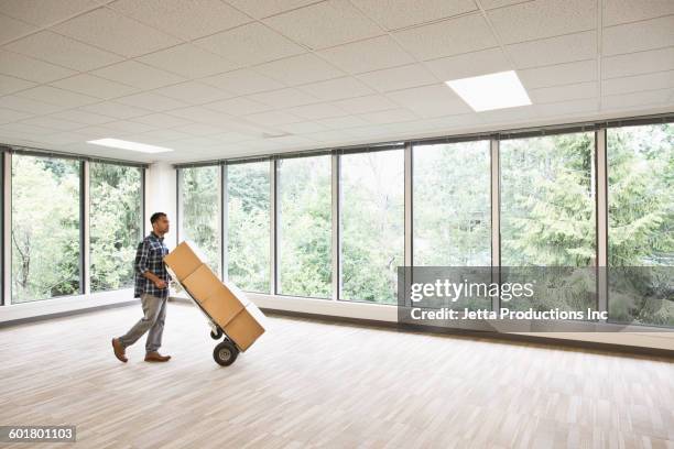 mixed race businessman wheeling boxes in empty office - sackkarre stock-fotos und bilder