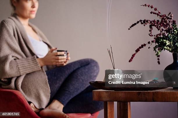 caucasian woman burning incense in living room - wierook gefabriceerd object stockfoto's en -beelden
