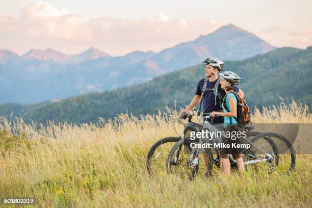 caucasian couple riding mountain bikes in field - bicycle and couple stockfoto's en -beelden