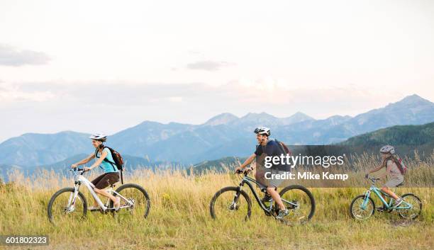 caucasian family riding mountain bikes in field - family bicycle stock pictures, royalty-free photos & images