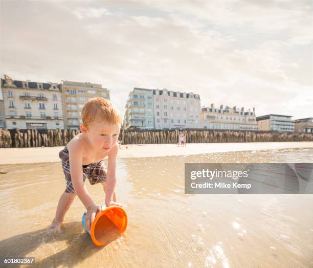 caucasian boy catching water in pail on beach - st malo stock pictures, royalty-free photos & images